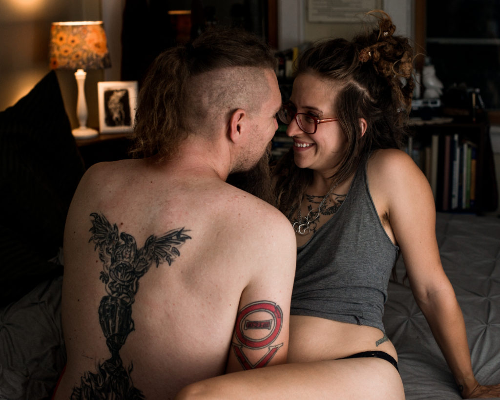 couple sitting on bed during a boudoir photography session in a bedroom. the man and woman both have tattoos