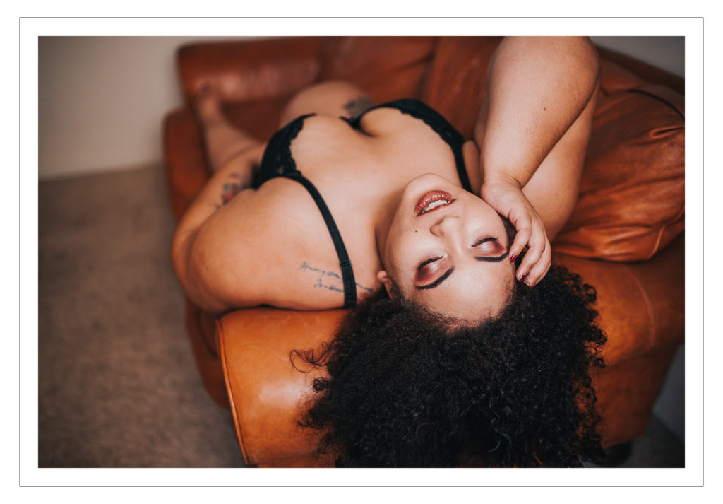 plus size boudoir portrait of a woman of color laying on her back on a n orange couch. This portrait is taken by body positive Michigan photographer Madelin Zaycheck who resides in Upper Peninsula Michigan 